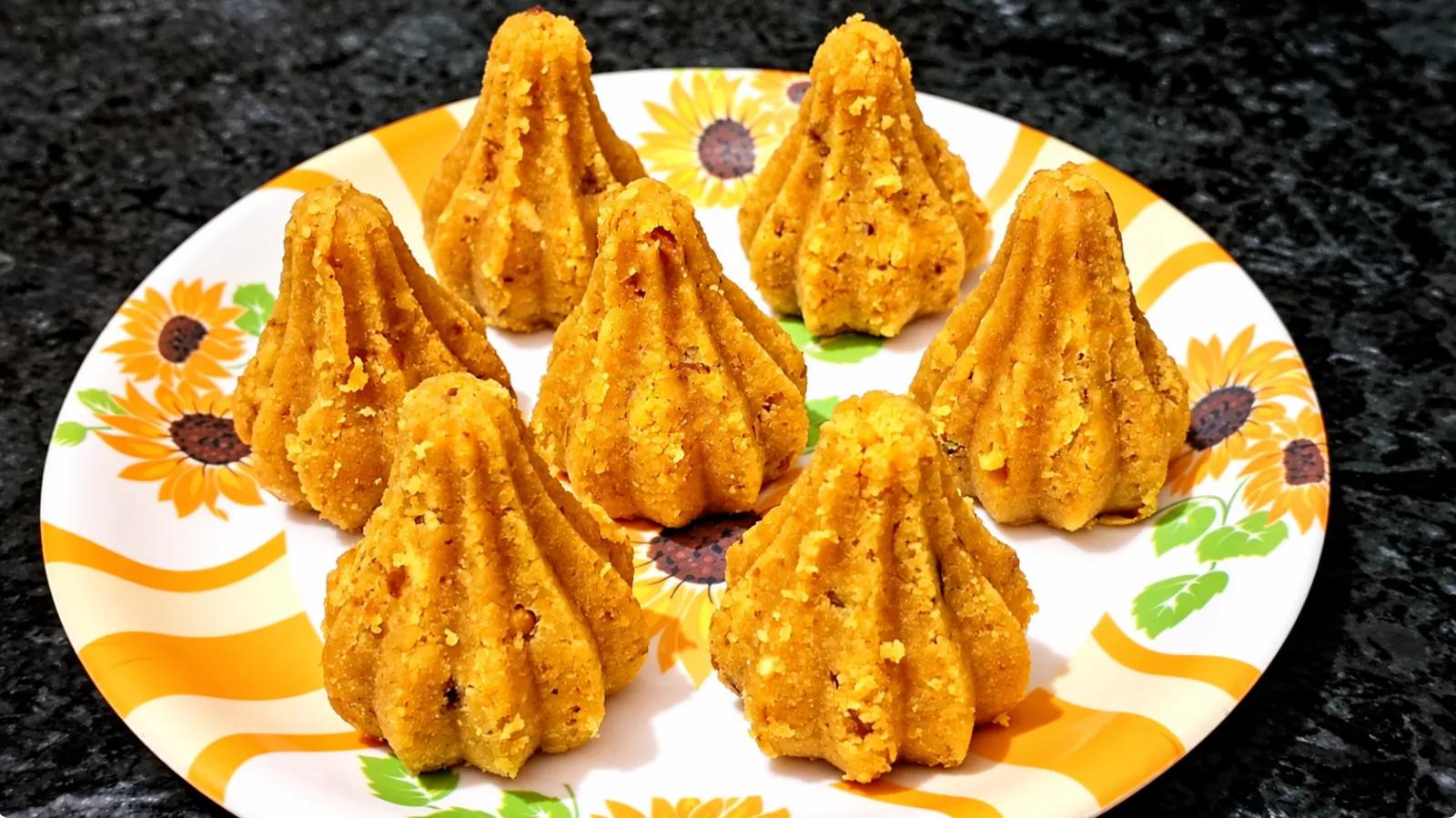 Golden besan modaks arranged on a floral serving plate against a dark stone counter.